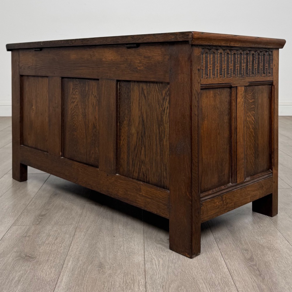 A rectangular dark oak blanket box featuring a hinged top lid, panelled front sections, and carved arch motifs along the upper frieze. View VI