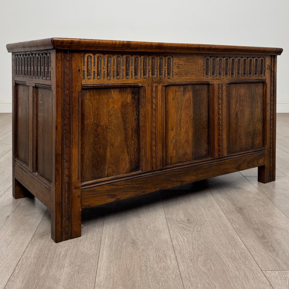 A rectangular dark oak blanket box featuring a hinged top lid, panelled front sections, and carved arch motifs along the upper frieze. View VIII