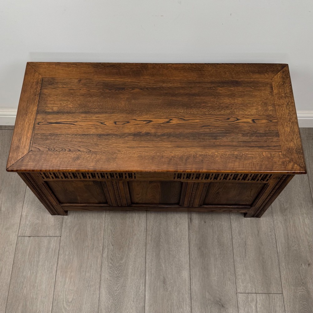 A rectangular dark oak blanket box featuring a hinged top lid, panelled front sections, and carved arch motifs along the upper frieze. View IX