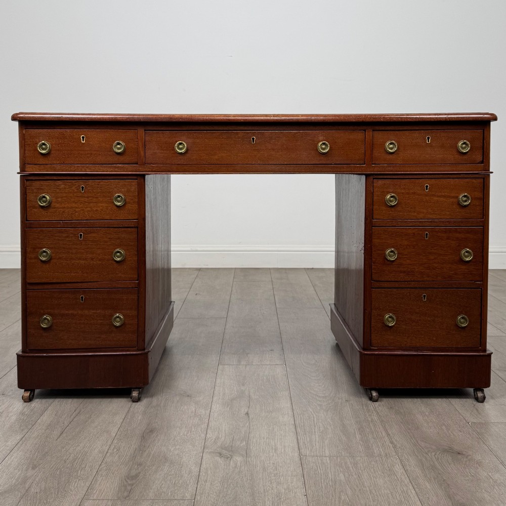 A 19th-century Victorian mahogany pedestal desk featuring nine drawers with circular brass knobs and keyholes, supported by twin plinth bases on casters.