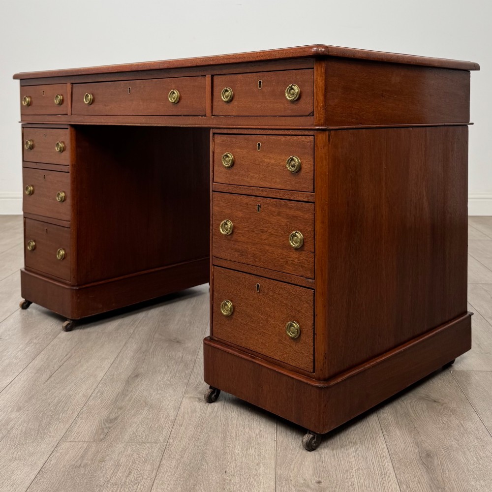 A 19th-century Victorian mahogany pedestal desk featuring nine drawers with circular brass knobs and keyholes, supported by twin plinth bases on casters. View II