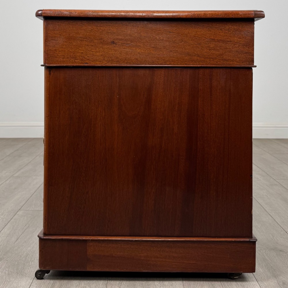 A 19th-century Victorian mahogany pedestal desk featuring nine drawers with circular brass knobs and keyholes, supported by twin plinth bases on casters. View III