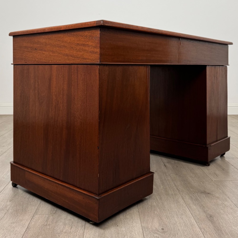 A 19th-century Victorian mahogany pedestal desk featuring nine drawers with circular brass knobs and keyholes, supported by twin plinth bases on casters. View IV