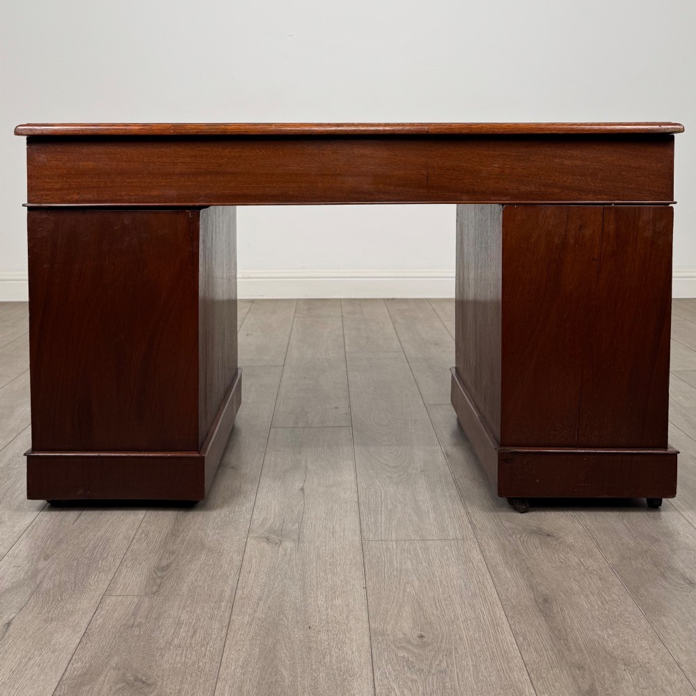 A 19th-century Victorian mahogany pedestal desk featuring nine drawers with circular brass knobs and keyholes, supported by twin plinth bases on casters. View V