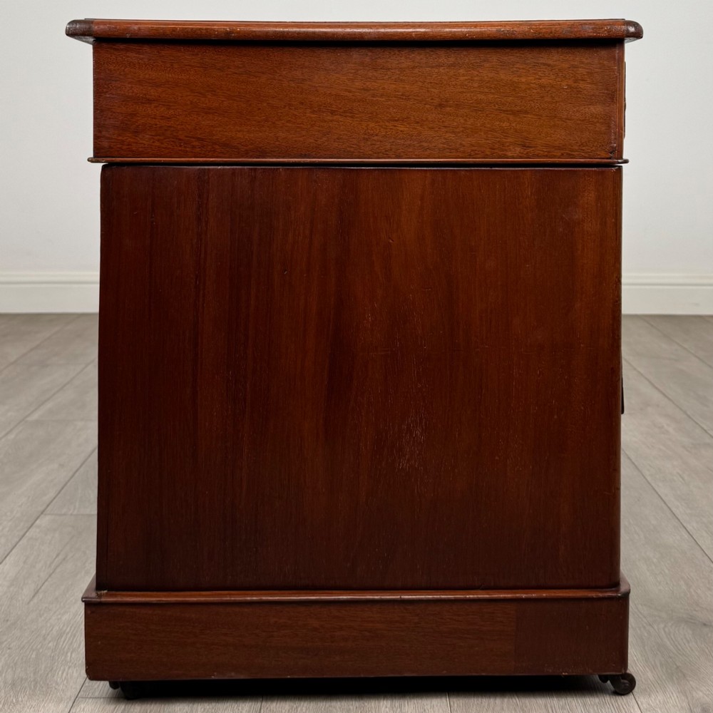 A 19th-century Victorian mahogany pedestal desk featuring nine drawers with circular brass knobs and keyholes, supported by twin plinth bases on casters. View VII