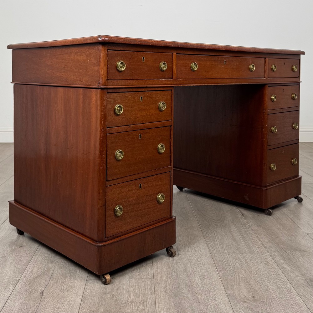 A 19th-century Victorian mahogany pedestal desk featuring nine drawers with circular brass knobs and keyholes, supported by twin plinth bases on casters. View VIII