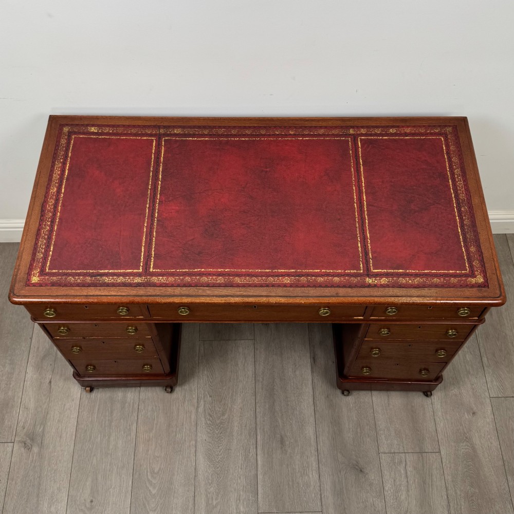 A 19th-century Victorian mahogany pedestal desk featuring nine drawers with circular brass knobs and keyholes, supported by twin plinth bases on casters. View IX