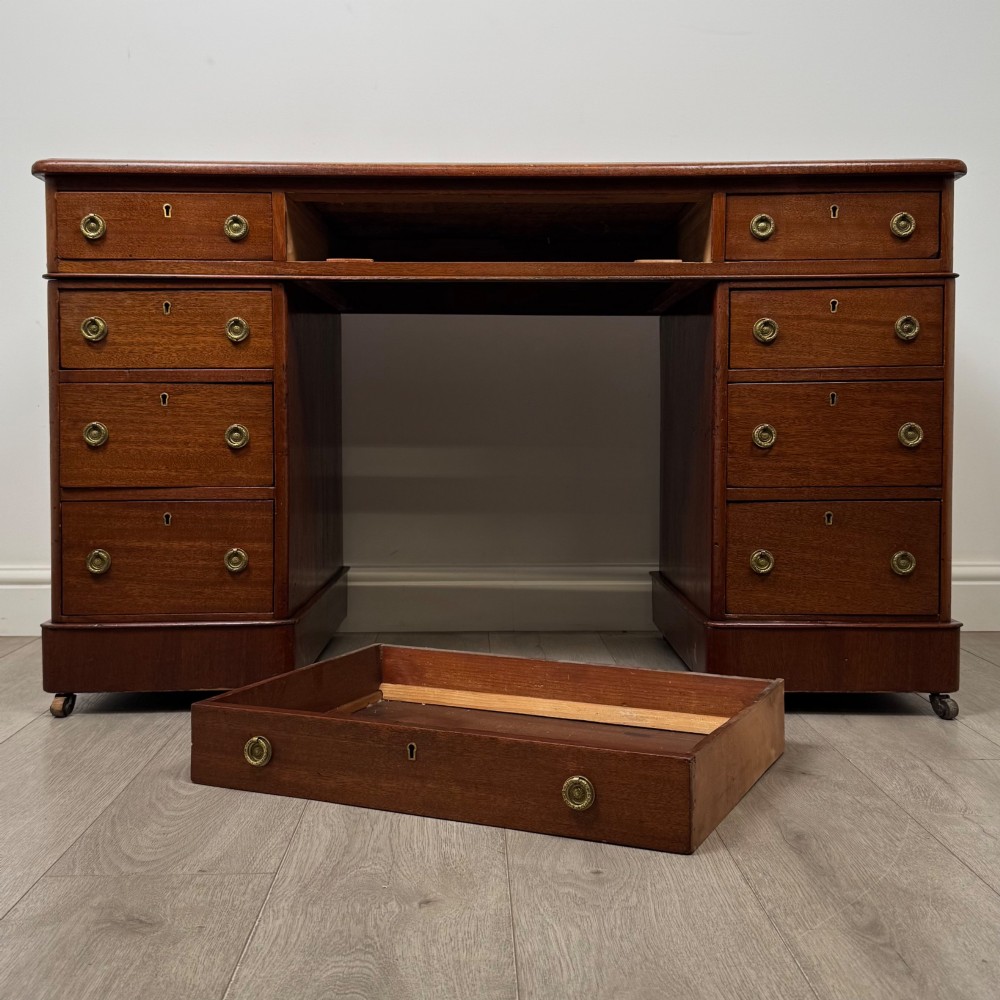 A 19th-century Victorian mahogany pedestal desk featuring nine drawers with circular brass knobs and keyholes, supported by twin plinth bases on casters. View X