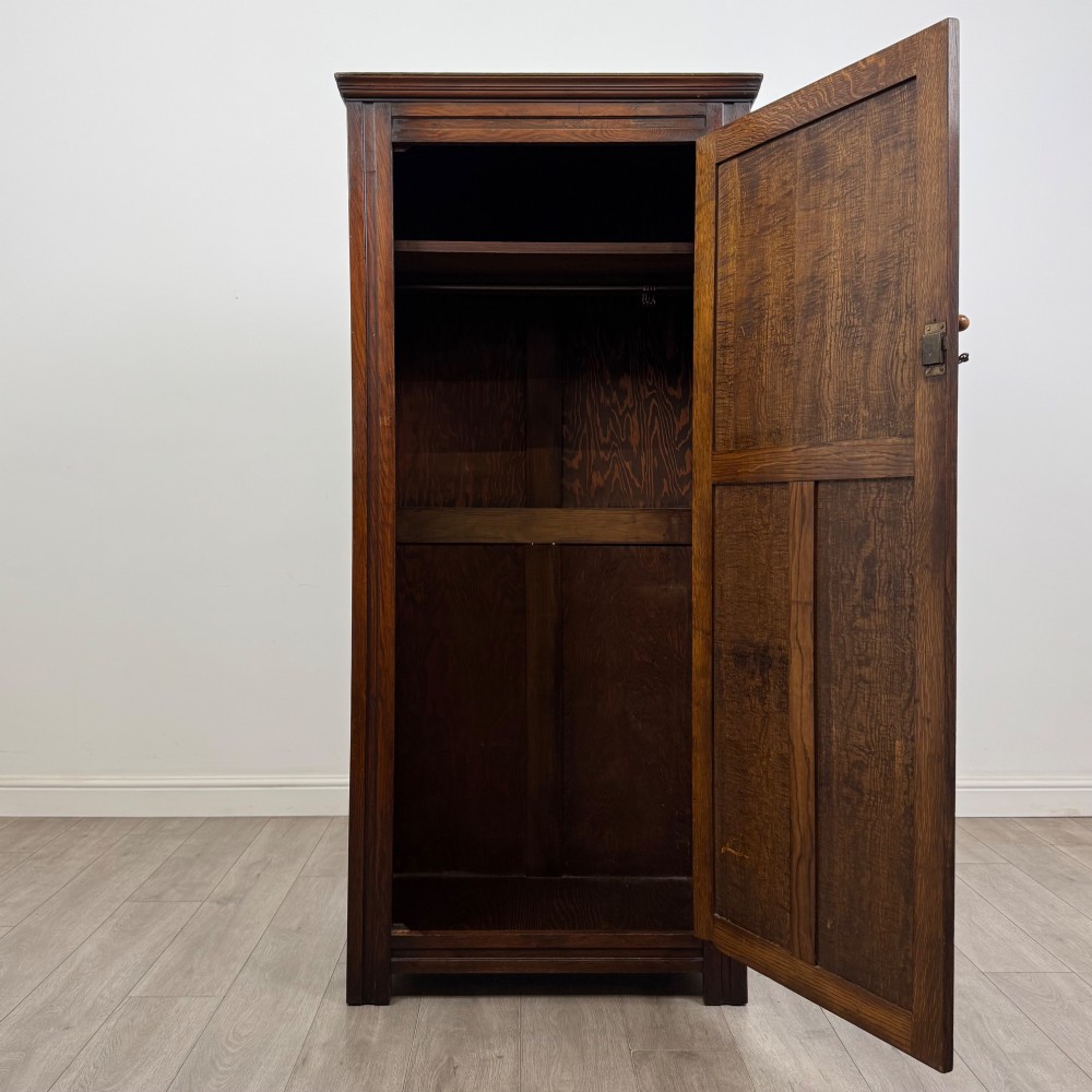 A tall single-door dark oak Edwardian wardrobe featuring a carved upper linenfold panel and decorative iron hinges. View II