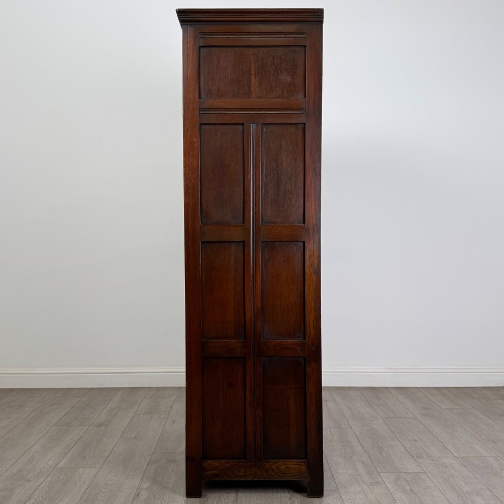 A tall single-door dark oak Edwardian wardrobe featuring a carved upper linenfold panel and decorative iron hinges. View IV