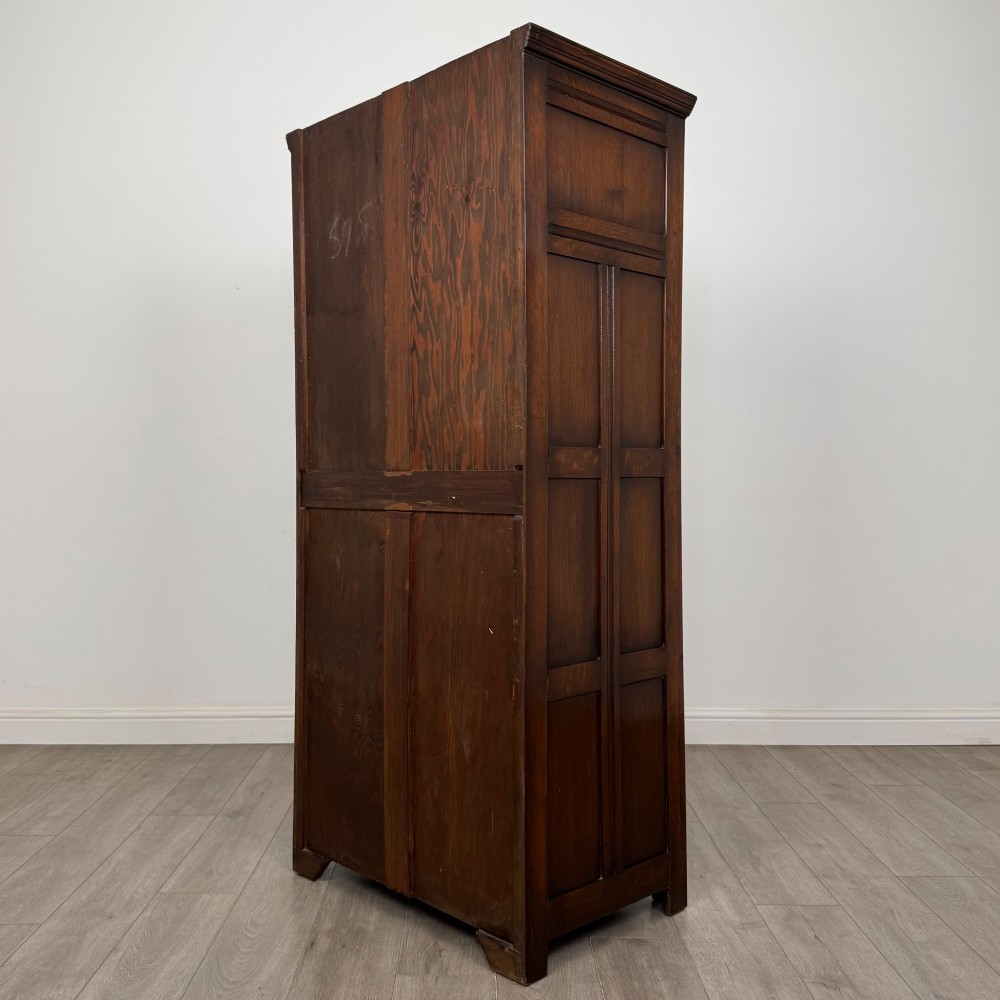 A tall single-door dark oak Edwardian wardrobe featuring a carved upper linenfold panel and decorative iron hinges. View VII