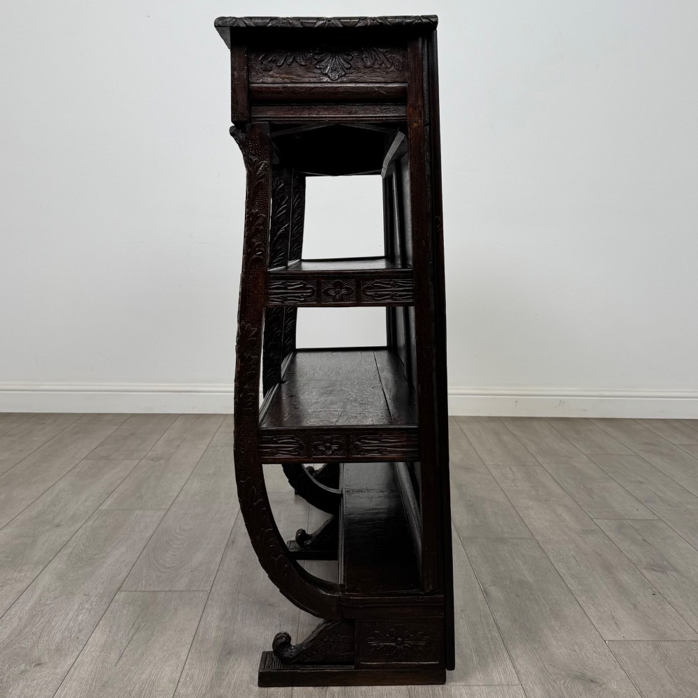 A 19th-century dark oak open bookcase featuring hand-carved frieze foliage, a central mask motif, and three tiers of open shelving. View III