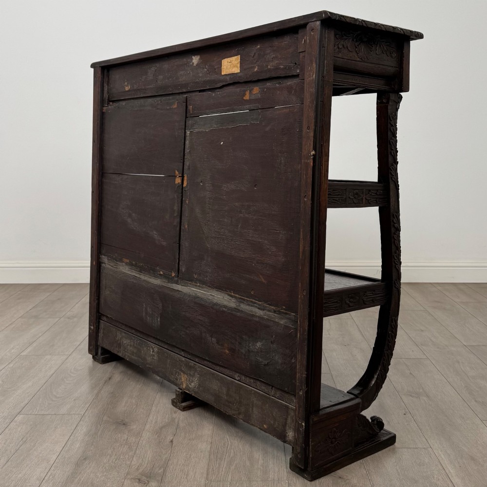 A 19th-century dark oak open bookcase featuring hand-carved frieze foliage, a central mask motif, and three tiers of open shelving. View VI