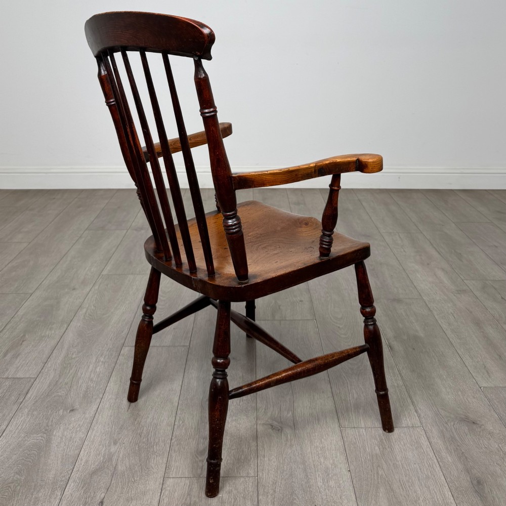 An antique 19th-century oak stick back armchair featuring turned spindle backrests, curved wooden armrests, a contoured solid seat, and turned legs joined by stretchers. View V