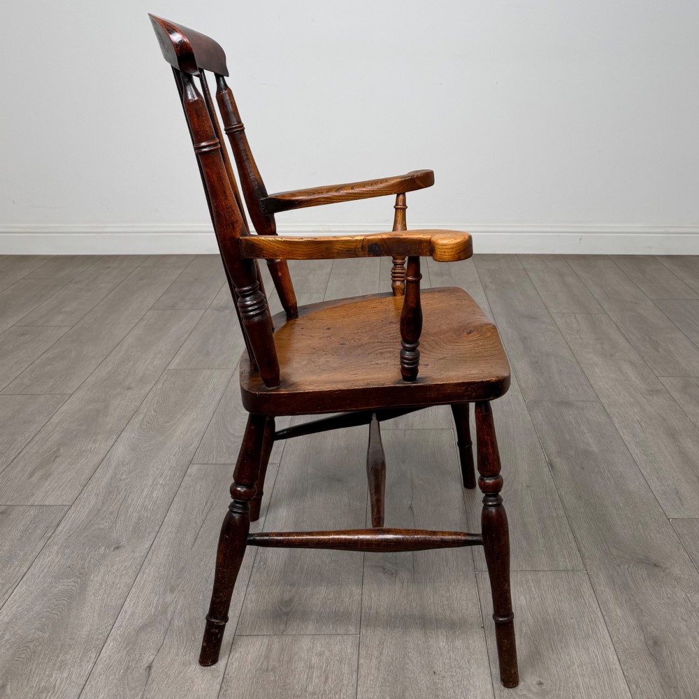 An antique 19th-century oak stick back armchair featuring turned spindle backrests, curved wooden armrests, a contoured solid seat, and turned legs joined by stretchers. View VI