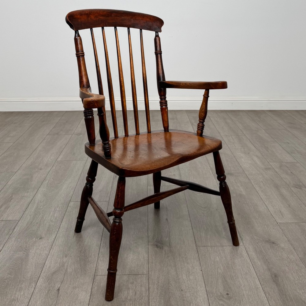 An antique 19th-century oak stick back armchair featuring turned spindle backrests, curved wooden armrests, a contoured solid seat, and turned legs joined by stretchers. View VII