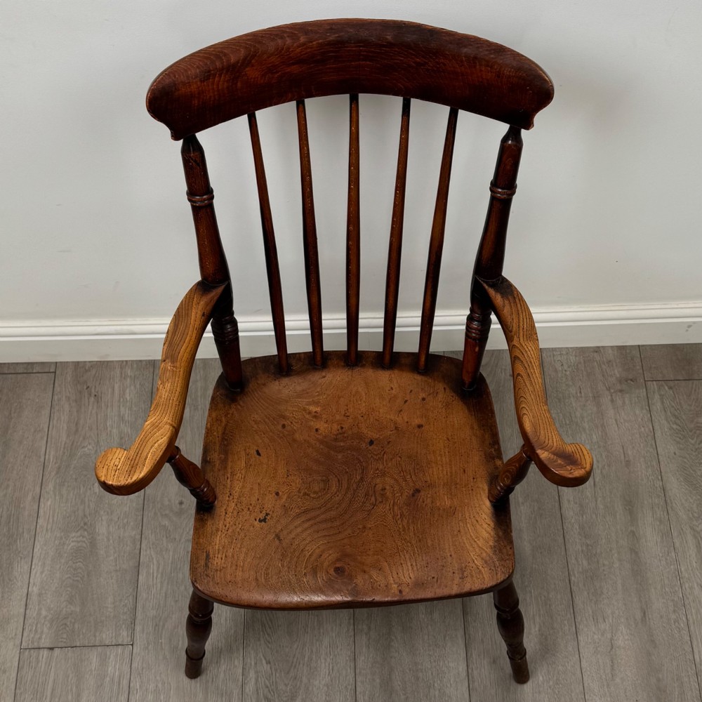 An antique 19th-century oak stick back armchair featuring turned spindle backrests, curved wooden armrests, a contoured solid seat, and turned legs joined by stretchers. View IX