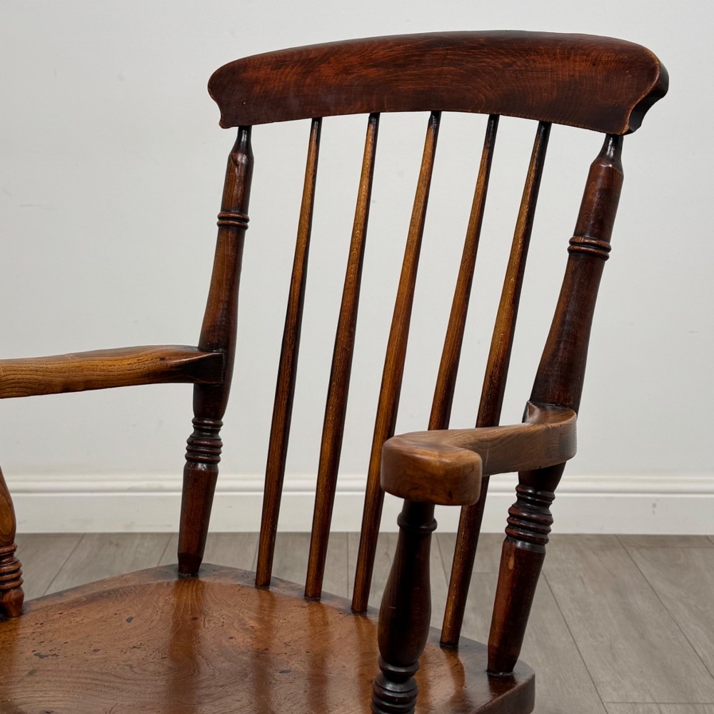 An antique 19th-century oak stick back armchair featuring turned spindle backrests, curved wooden armrests, a contoured solid seat, and turned legs joined by stretchers. View X