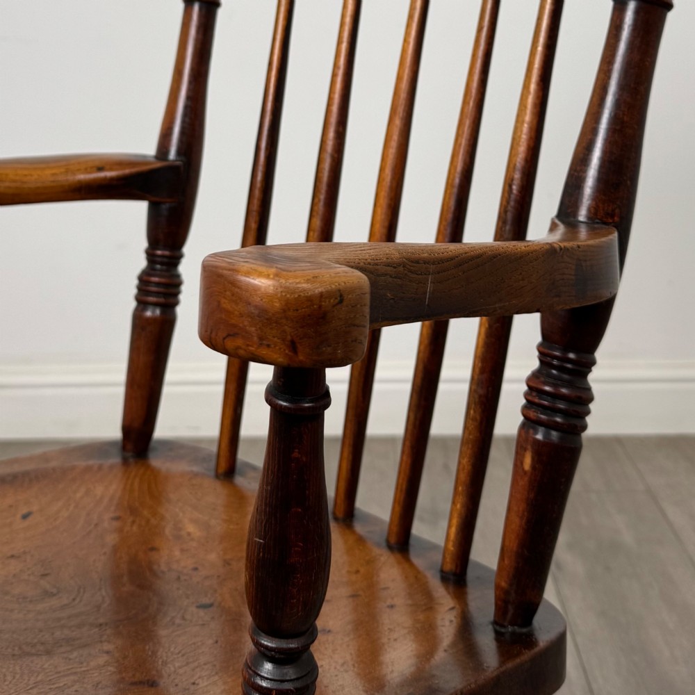 An antique 19th-century oak stick back armchair featuring turned spindle backrests, curved wooden armrests, a contoured solid seat, and turned legs joined by stretchers. View XII