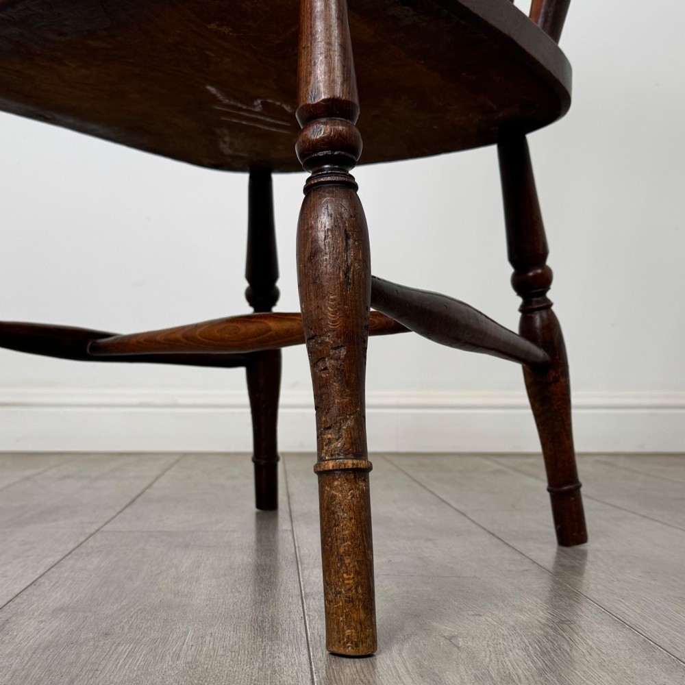 An antique 19th-century oak stick back armchair featuring turned spindle backrests, curved wooden armrests, a contoured solid seat, and turned legs joined by stretchers. View XIII