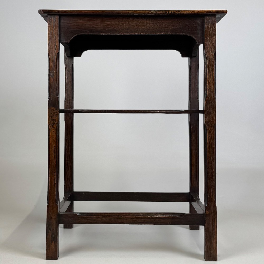 An Edwardian dark oak side table with a flat square top, lower tier shelf, shaped aprons, and straight square legs.