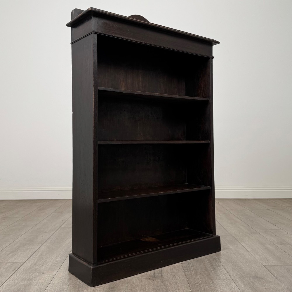 An Edwardian dark-stained oak open bookcase featuring four shelf tiers containing red leather-bound books against a white background. View IX