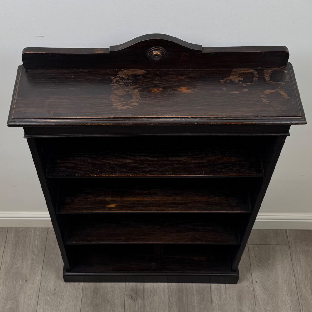 An Edwardian dark-stained oak open bookcase featuring four shelf tiers containing red leather-bound books against a white background. View X