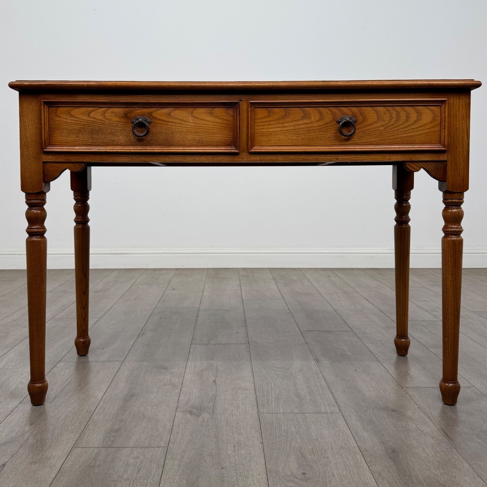 A 20th-century warm brown oak writing table featuring two frieze drawers with ring drop handles and four turned legs.