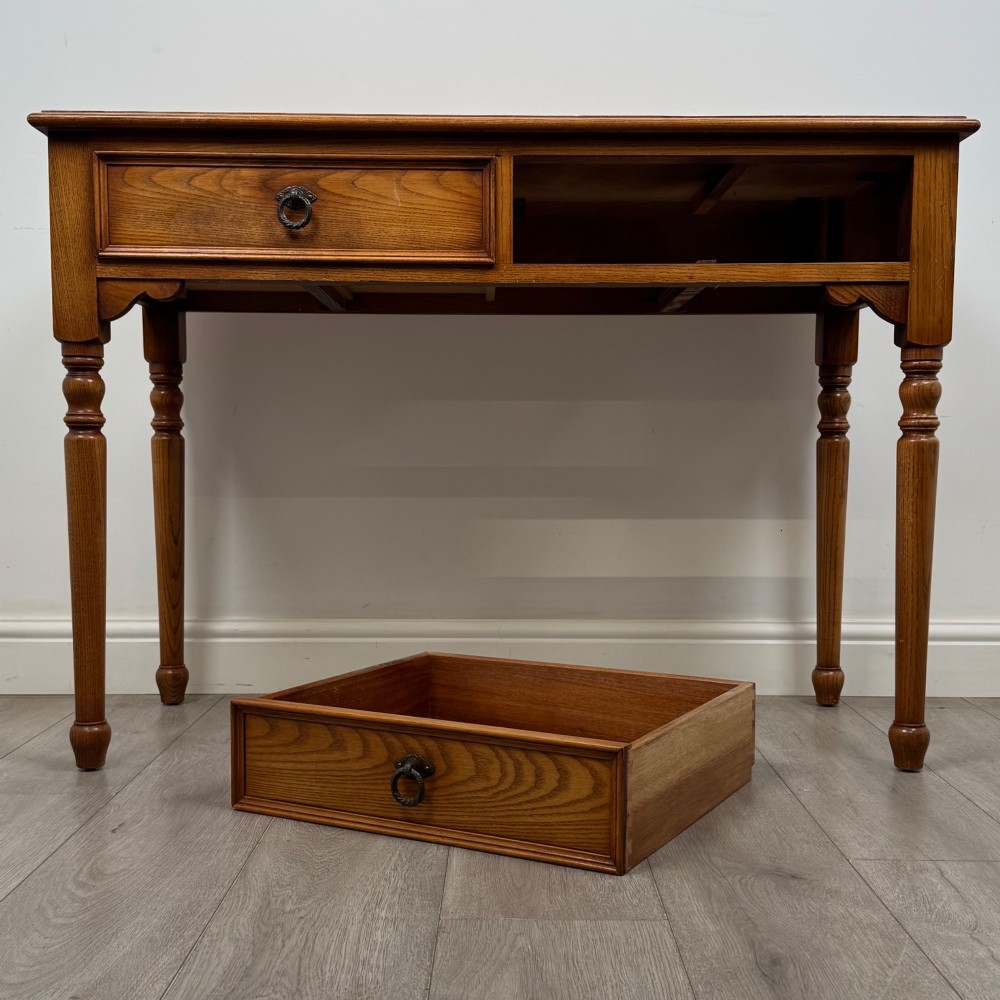 A 20th-century warm brown oak writing table featuring two frieze drawers with ring drop handles and four turned legs. View X