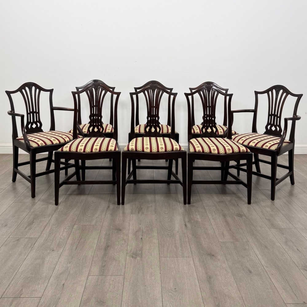 A set of eight dark mahogany shield back dining chairs, including two carvers and six side chairs, with striped red and cream upholstery.