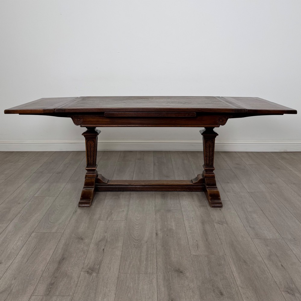 An Edwardian dark oak draw leaf dining table featuring extended side leaves, carved pedestal supports, and a low connecting stretcher. View II