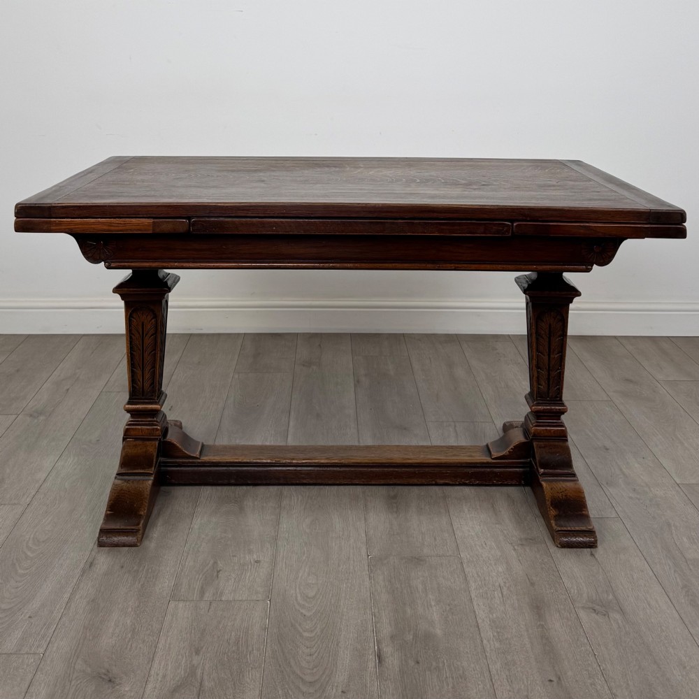 An Edwardian dark oak draw leaf dining table featuring extended side leaves, carved pedestal supports, and a low connecting stretcher. View III