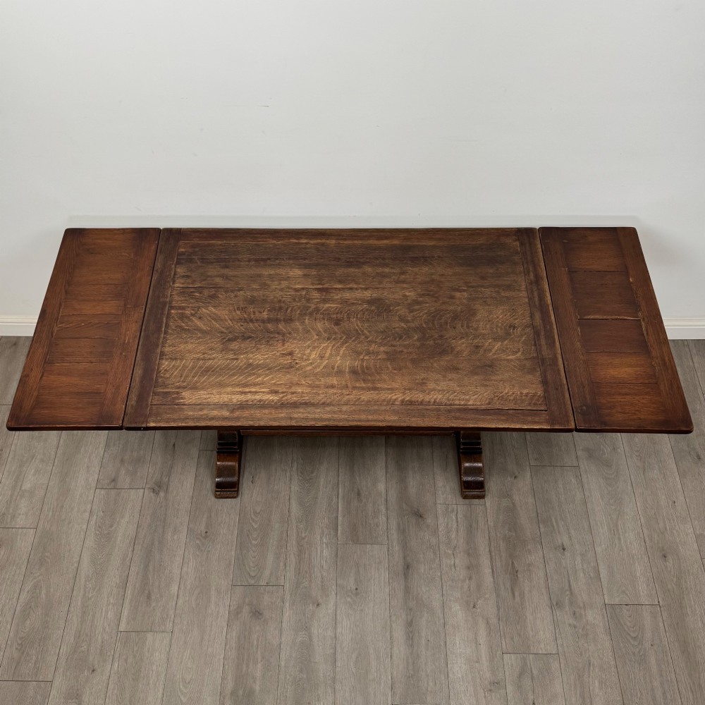 An Edwardian dark oak draw leaf dining table featuring extended side leaves, carved pedestal supports, and a low connecting stretcher. View VI