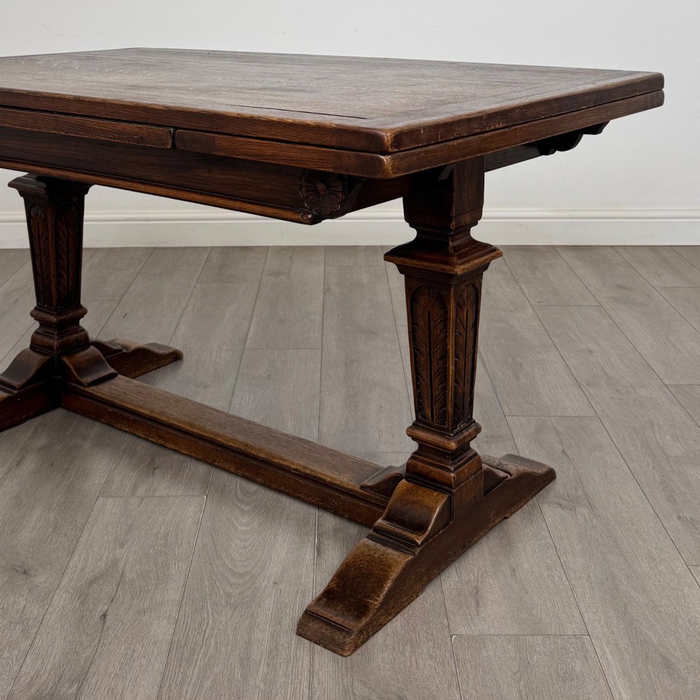 An Edwardian dark oak draw leaf dining table featuring extended side leaves, carved pedestal supports, and a low connecting stretcher. View VII