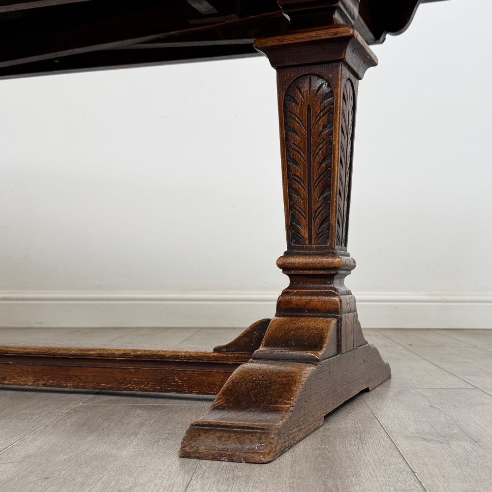An Edwardian dark oak draw leaf dining table featuring extended side leaves, carved pedestal supports, and a low connecting stretcher. View VIII