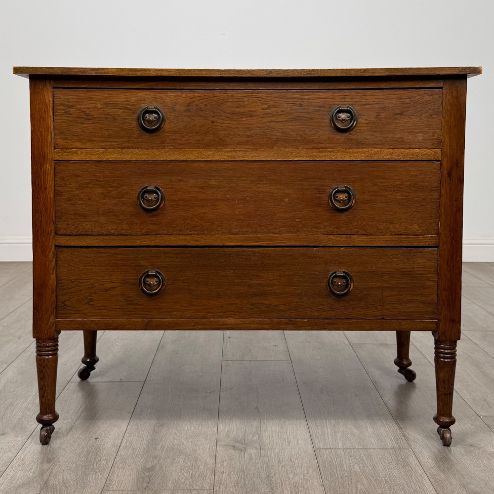 An antique Edwardian oak chest featuring three full-width drawers with brass ring drop handles, set on turned legs with castors.