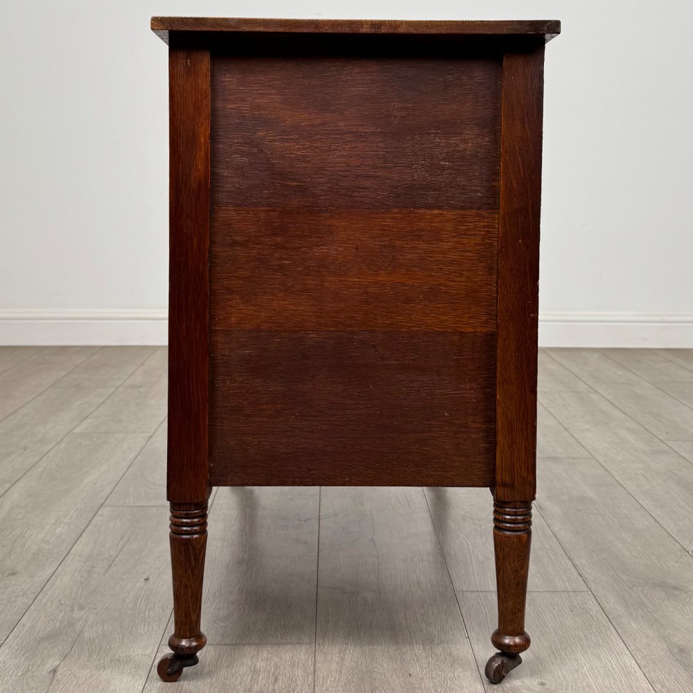 An antique Edwardian oak chest featuring three full-width drawers with brass ring drop handles, set on turned legs with castors. View III