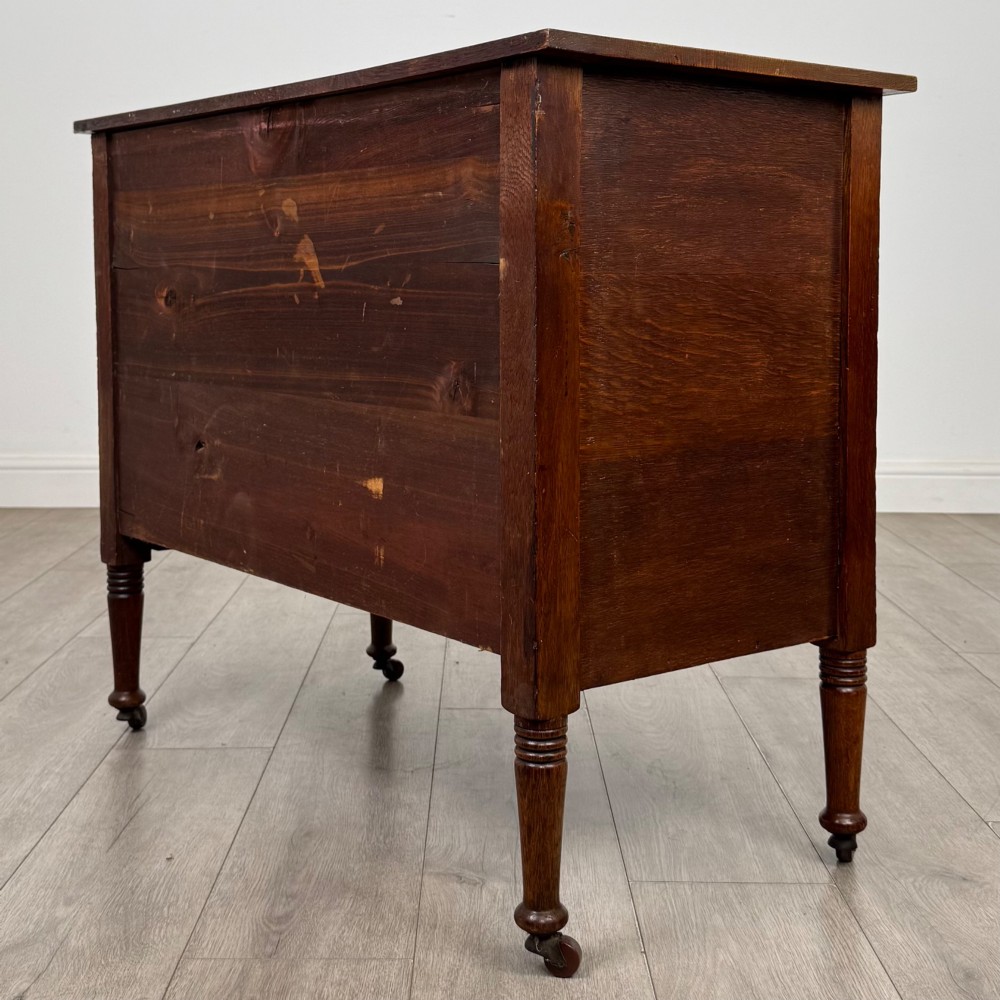 An antique Edwardian oak chest featuring three full-width drawers with brass ring drop handles, set on turned legs with castors. View VI