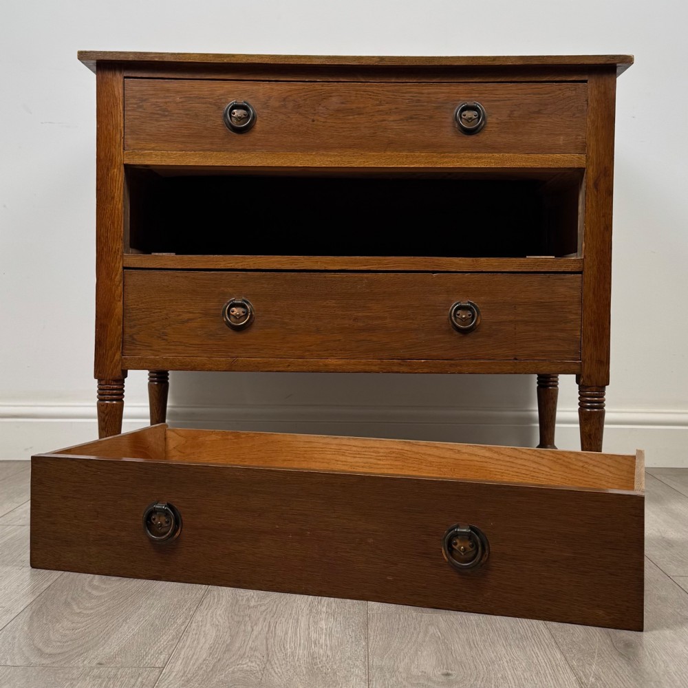 An antique Edwardian oak chest featuring three full-width drawers with brass ring drop handles, set on turned legs with castors. View X