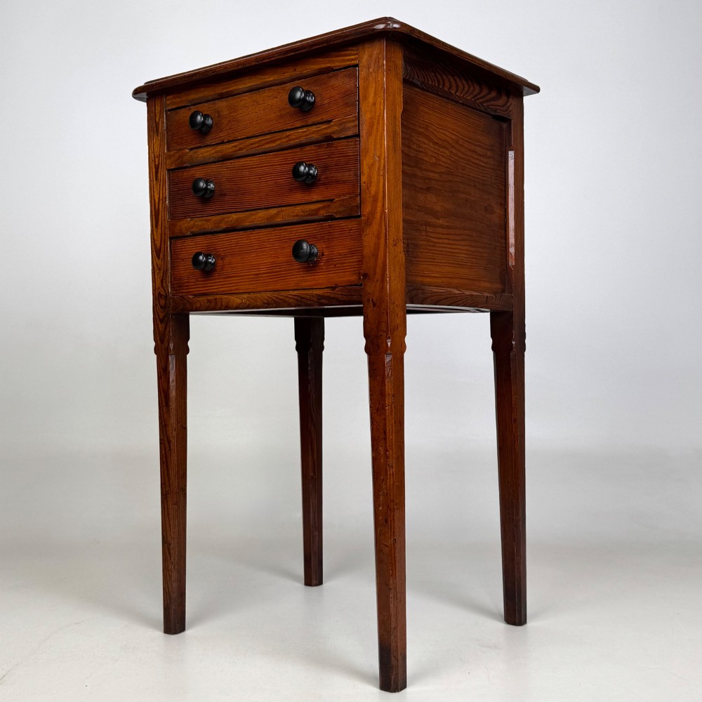 A Victorian pitch pine cabinet with three drawers and black wooden knobs set on elevated tapered square legs. View II
