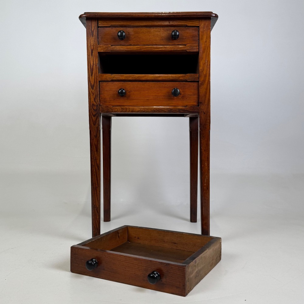 A Victorian pitch pine cabinet with three drawers and black wooden knobs set on elevated tapered square legs. View X