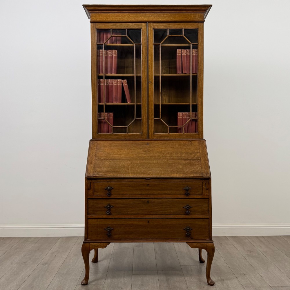 An Edwardian oak bureau bookcase with a two-door upper glazed display cabinet, a sloping drop-front desk, three wide drawers, and cabriole legs.