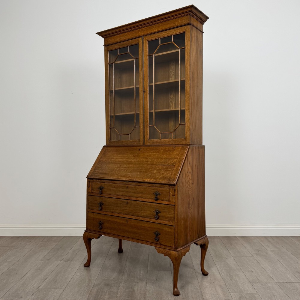 An Edwardian oak bureau bookcase with a two-door upper glazed display cabinet, a sloping drop-front desk, three wide drawers, and cabriole legs. View IV