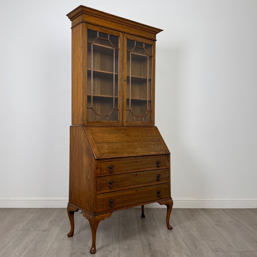An Edwardian oak bureau bookcase with a two-door upper glazed display cabinet, a sloping drop-front desk, three wide drawers, and cabriole legs. View X