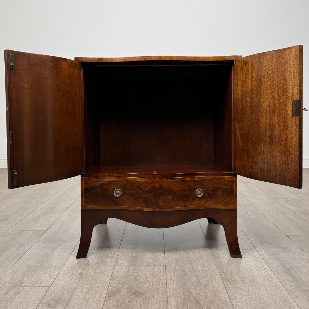 A 20th-century mahogany serpentine cupboard featuring flame mahogany oval door panels, chevron veneering, a lower drawer with brass ring handles, and splayed bracket feet. View II