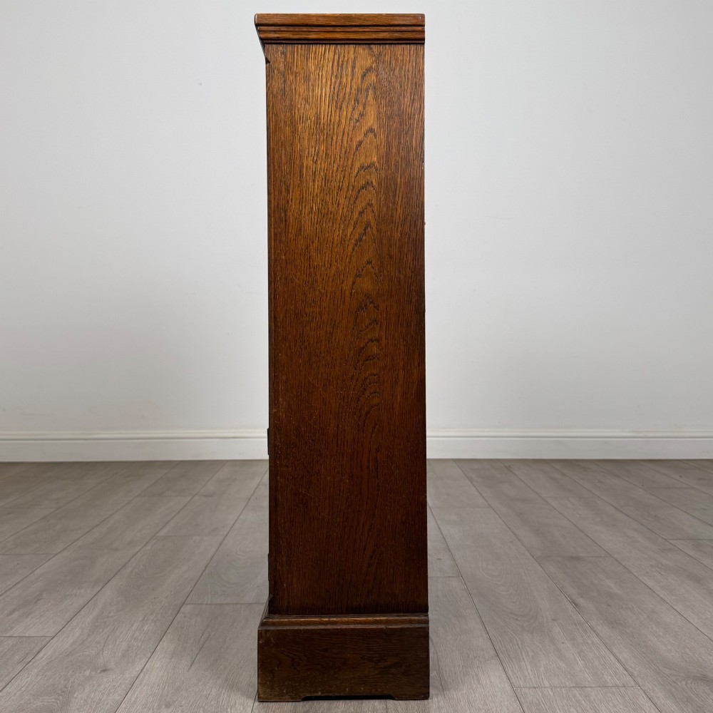 A small medium-brown oak open bookcase featuring two upper shelves and a lower two-door cupboard with carved arched motifs and metal ring handles. View V