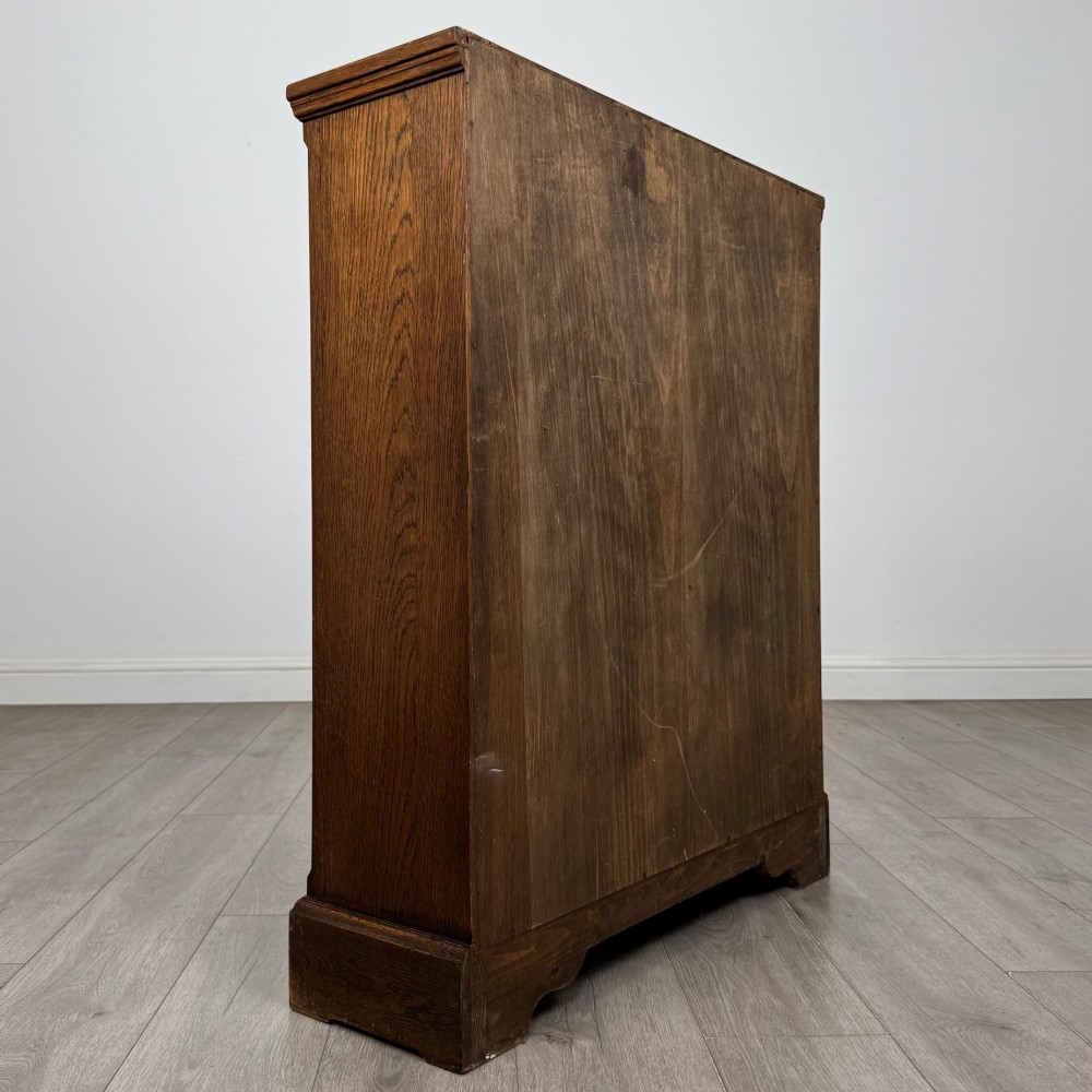 A small medium-brown oak open bookcase featuring two upper shelves and a lower two-door cupboard with carved arched motifs and metal ring handles. View VI