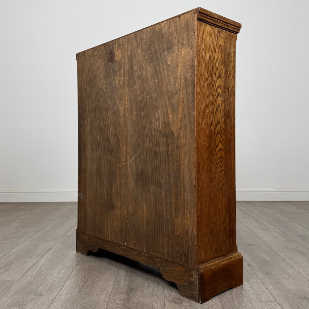 A small medium-brown oak open bookcase featuring two upper shelves and a lower two-door cupboard with carved arched motifs and metal ring handles. View VIII