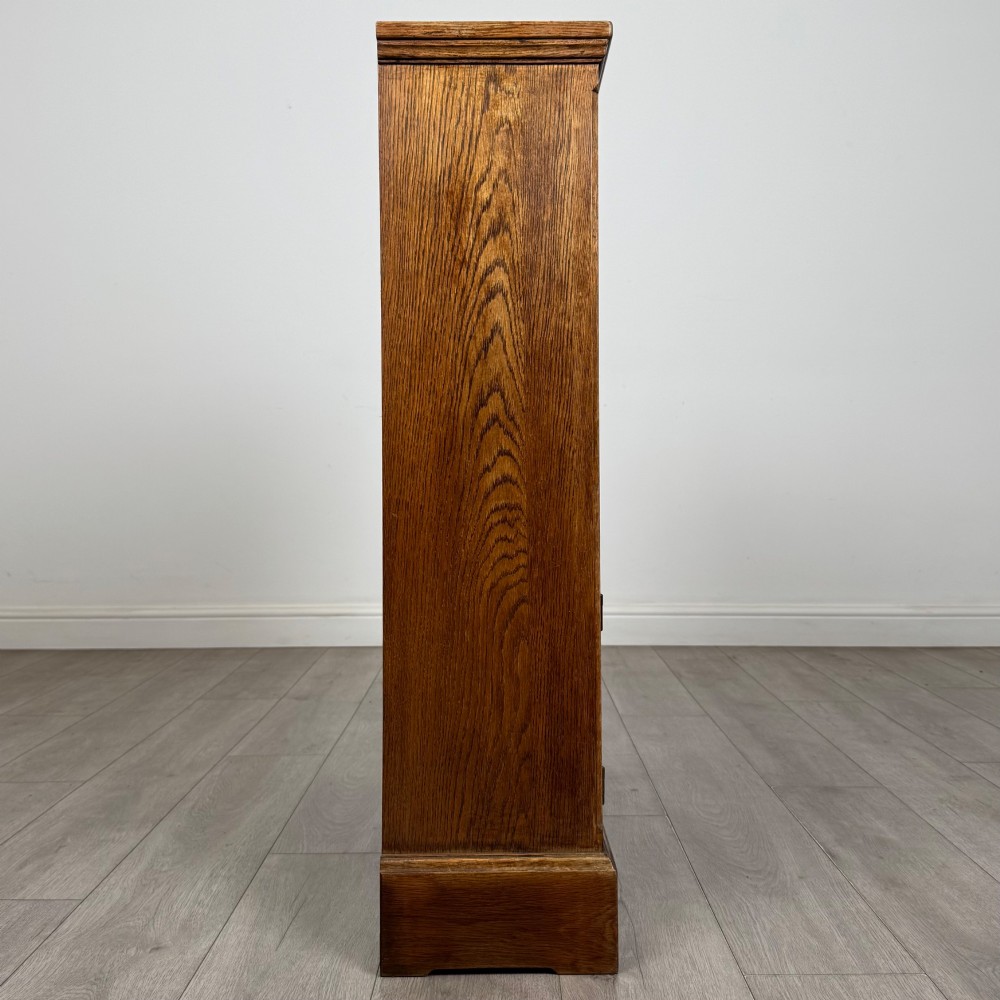 A small medium-brown oak open bookcase featuring two upper shelves and a lower two-door cupboard with carved arched motifs and metal ring handles. View IX