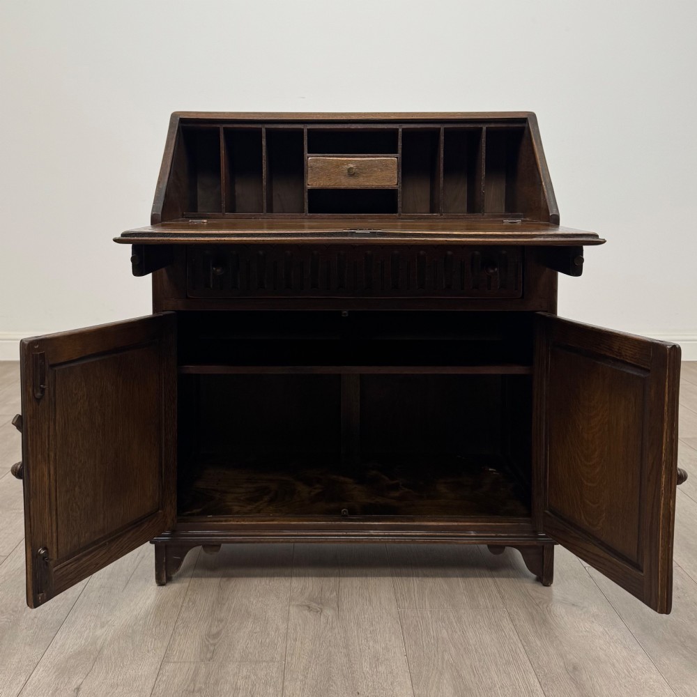 A dark oak slant-front writing bureau featuring carved linenfold upper panels, a single carved drawer with wooden knobs, and a double-door cupboard base decorated with diamond lozenge carvings. View II